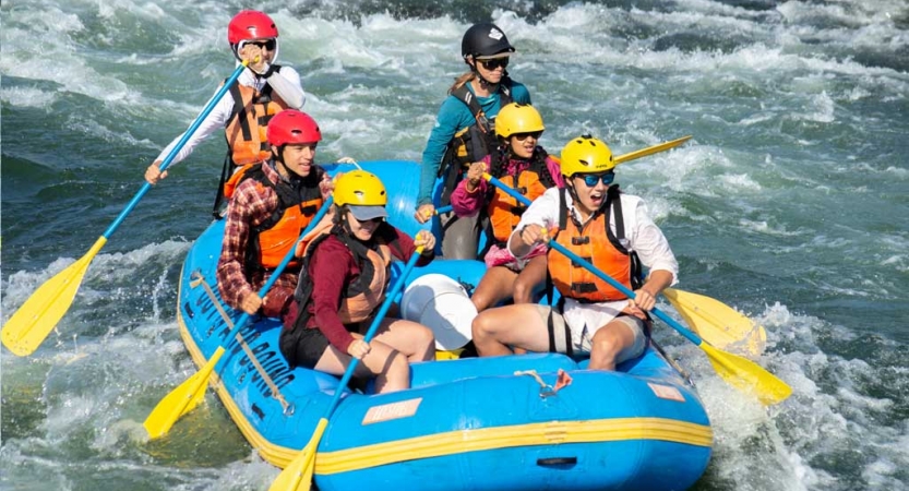 a group outward bound students use paddles as they guide a raft through whitewater 